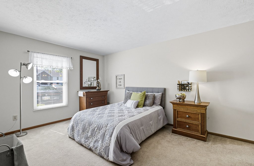 A bedroom with a bed, nightstand, and window.