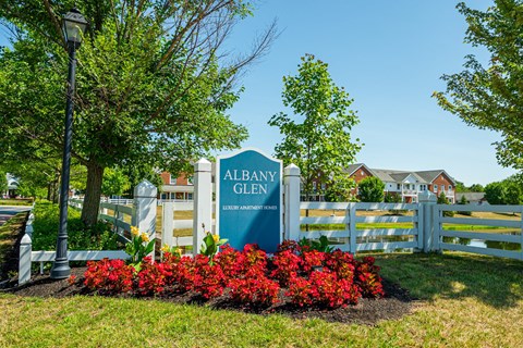 a sign for albany glen in front of a fence and red flowers