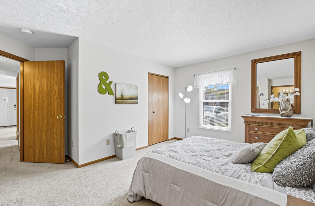 A bedroom with a large bed and a mirror on the dresser.