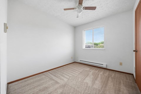 A room with a ceiling fan and a window with a view of trees and a fence outside.