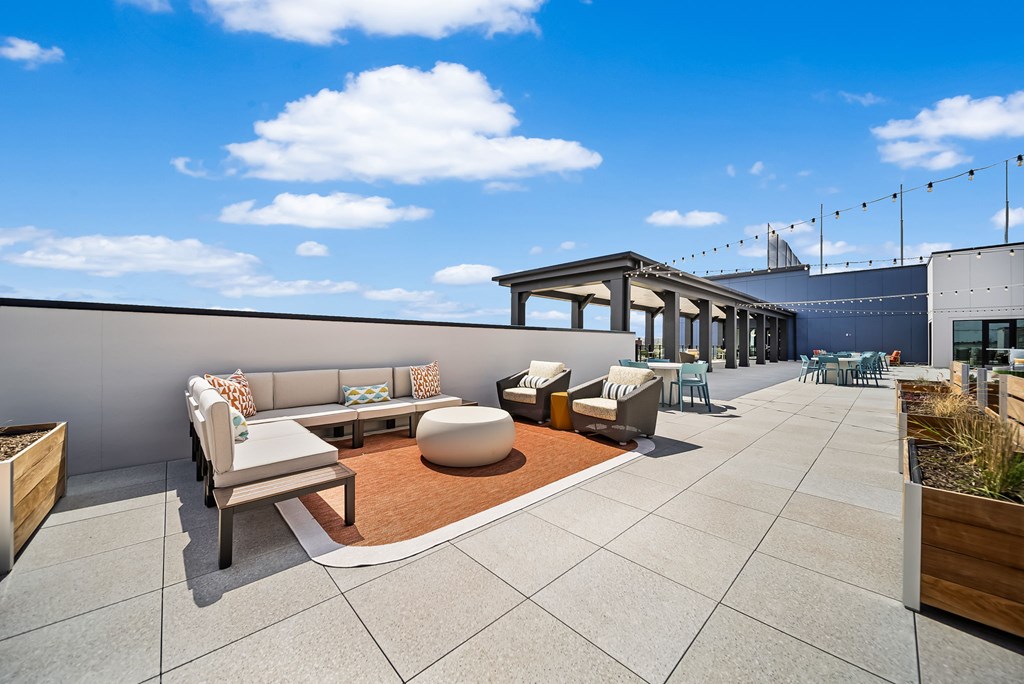 A rooftop patio with a white couch, a brown rug, and a wooden table.