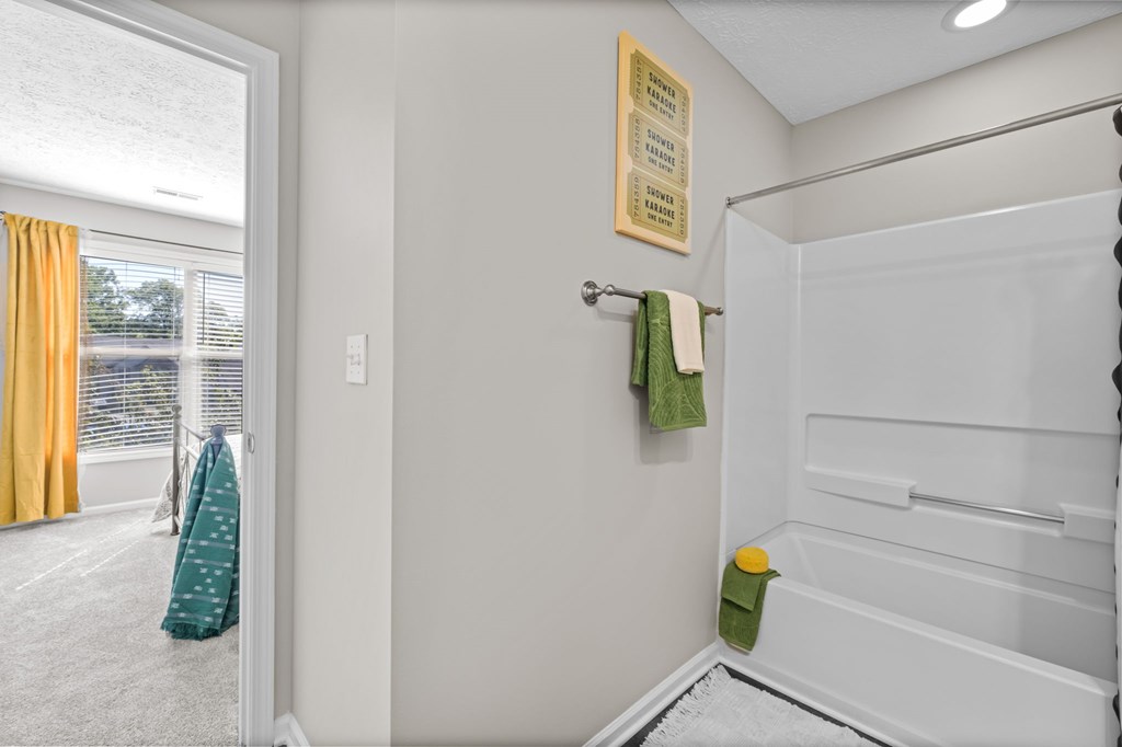 A bathroom with a white tub and a green towel hanging on the door.