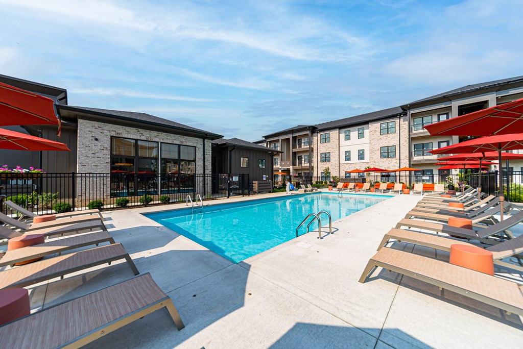 A swimming pool surrounded by sun loungers and apartment buildings.
