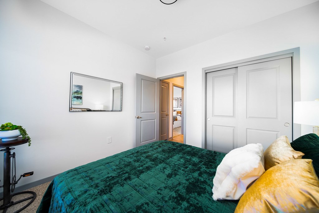 A bedroom with a green bedspread and a white dog on the bed.