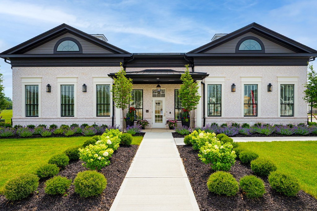 A house with a white facade and a grey roof with a garden in front.