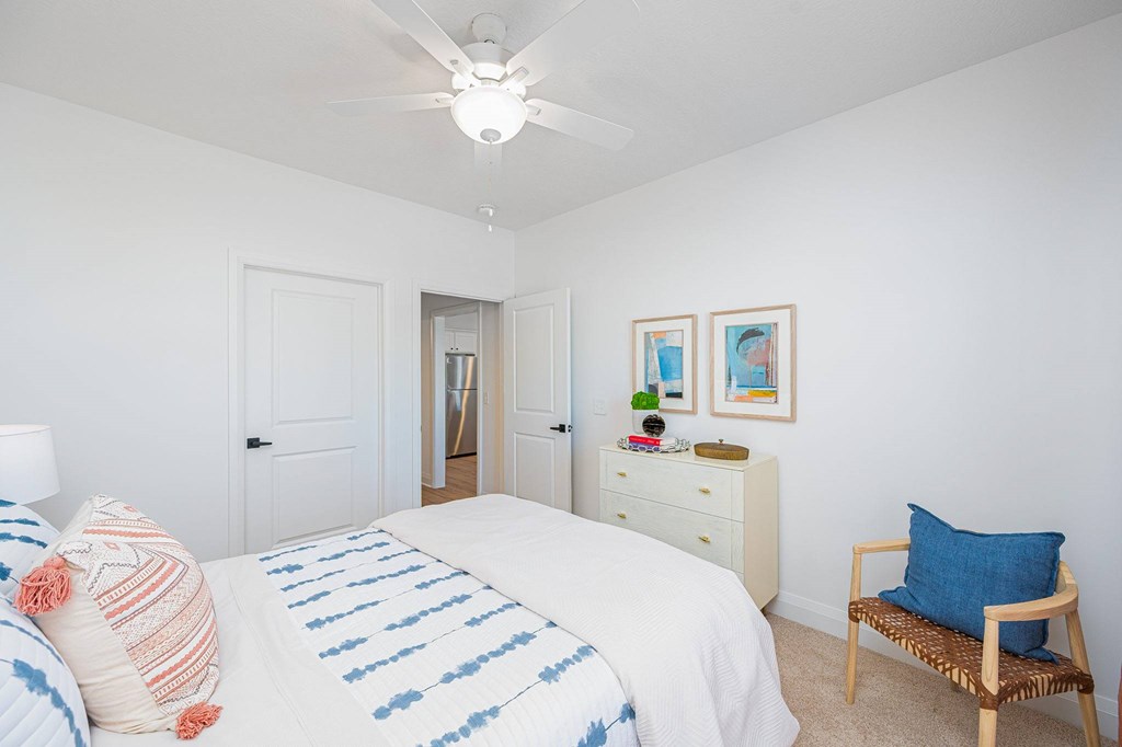 A bedroom with a bed, pillows, a ceiling fan, and a chair.
