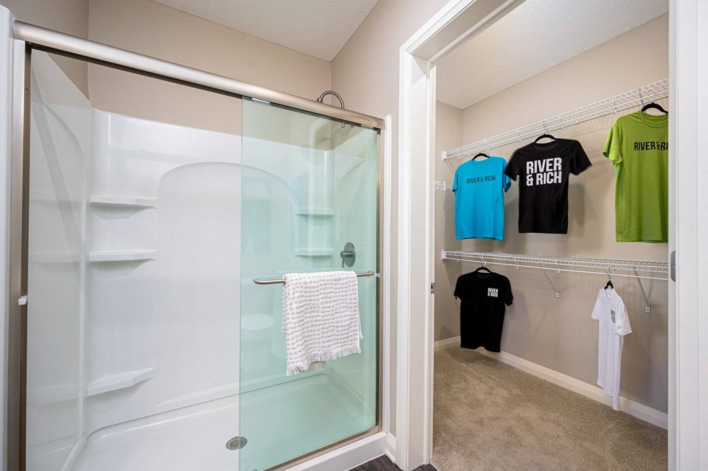 a walk in closet with a glass shower and shirts hanging on the wall