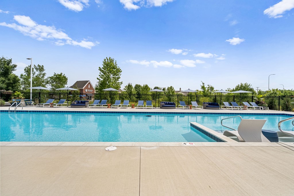 A large swimming pool with lounge chairs and a fence in the background.