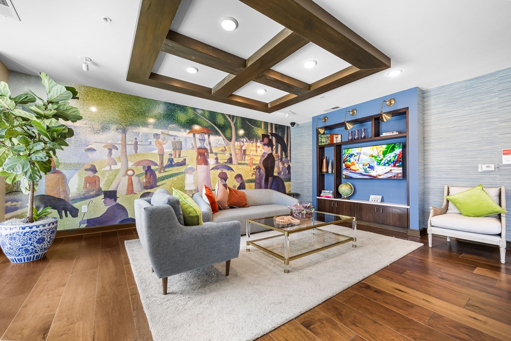 A living room with a grey sofa, a white armchair, a coffee table, and a large mural on the wall.