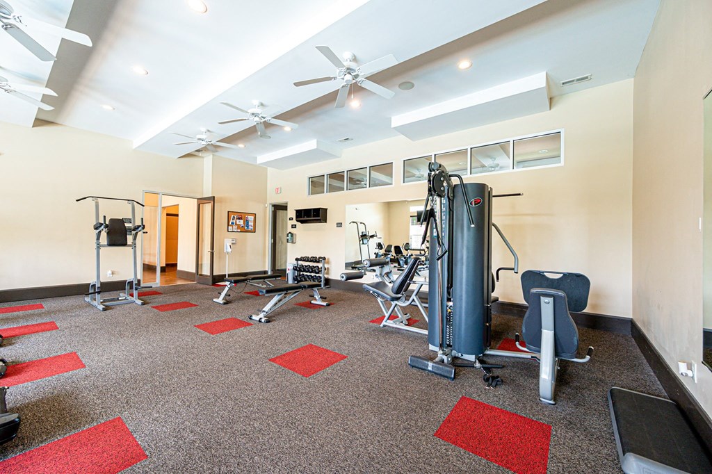 a gym with weights and cardio equipment on the floor and a ceiling fan