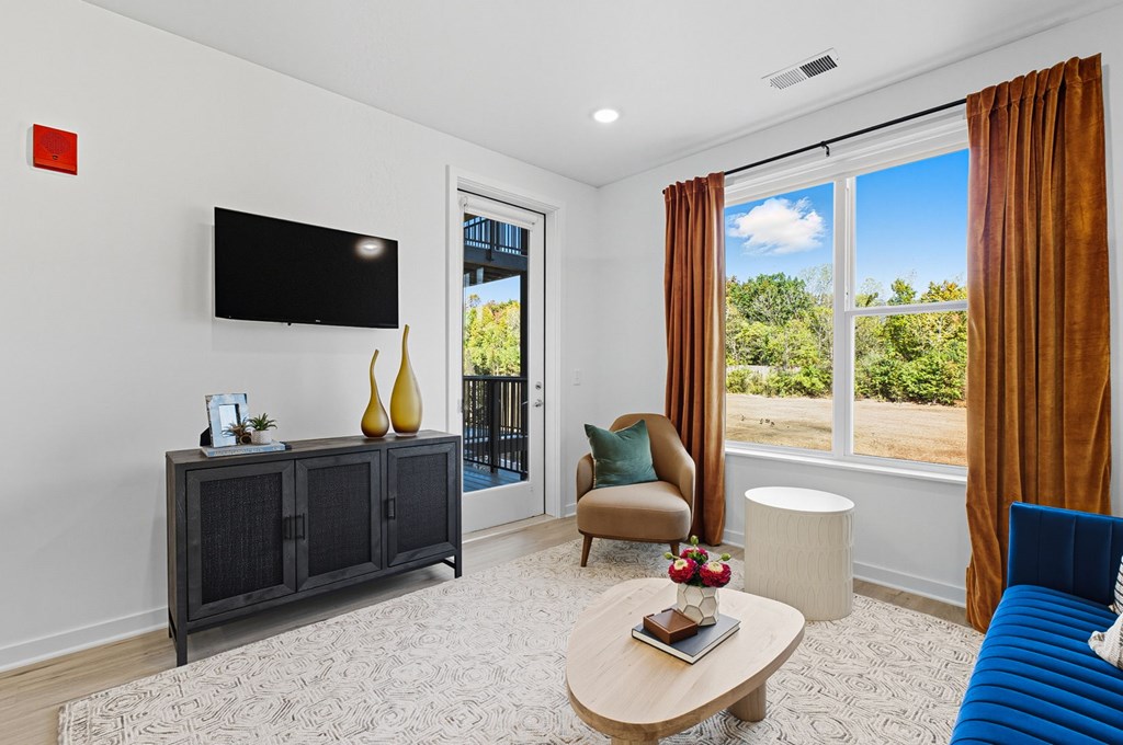 A living room with a blue sofa, a wooden coffee table, a flat screen TV, and a sliding glass door leading to a balcony.