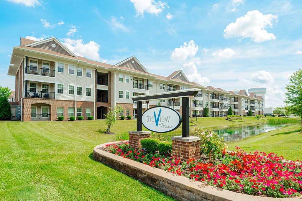 an apartment building with a sign in front of a pond and flowers