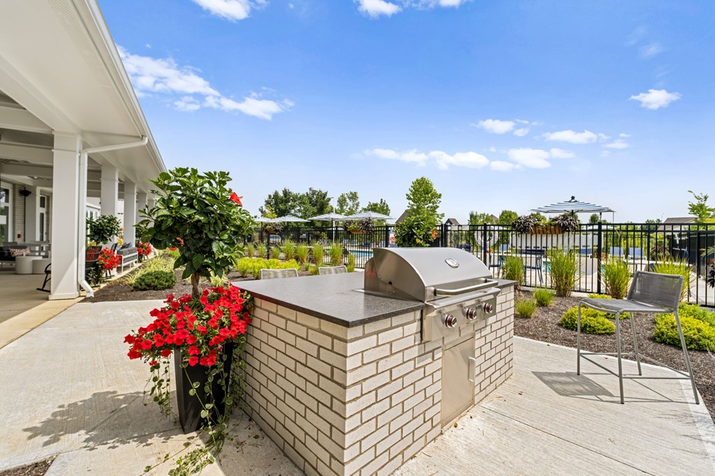 A brick BBQ is in a concrete patio in front of a house.
