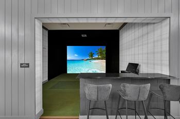 A room with a bar and chairs with a screen on the wall.