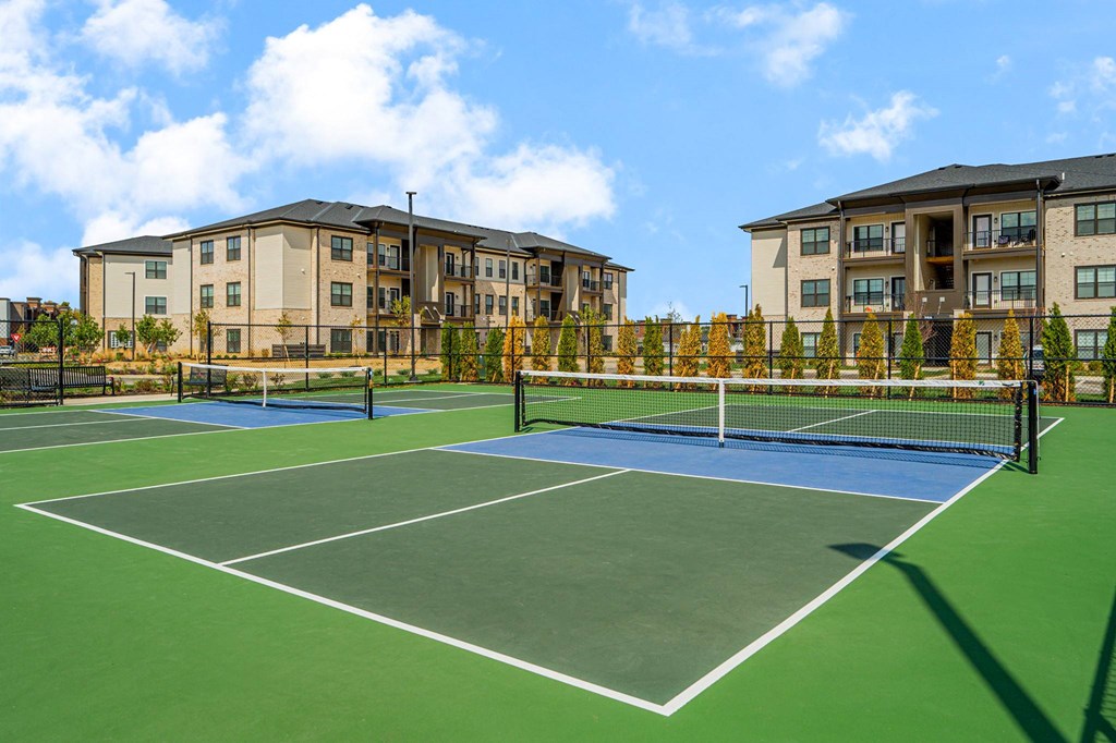A tennis court is surrounded by apartment buildings.