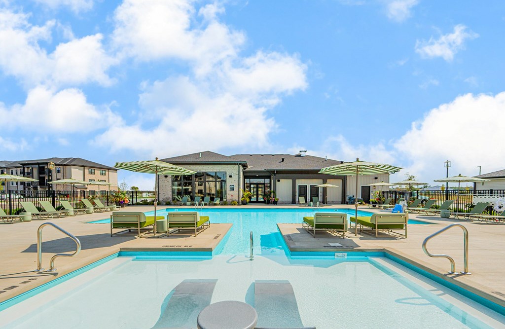 A large outdoor swimming pool with sun loungers and a building in the background.