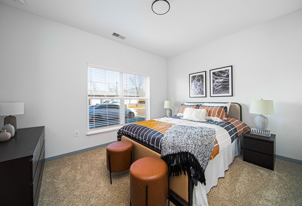 A bedroom with a bed, nightstand, and two stools.