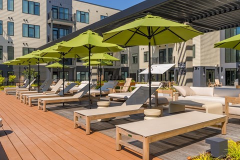 A row of lounge chairs and tables are set up on a wooden deck.