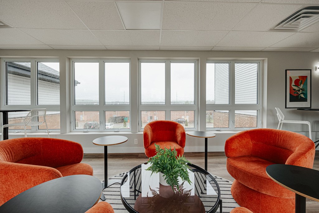 a living room with orange chairs and a table and windows