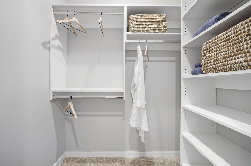 A white closet with clothes hanging and baskets on the shelves.