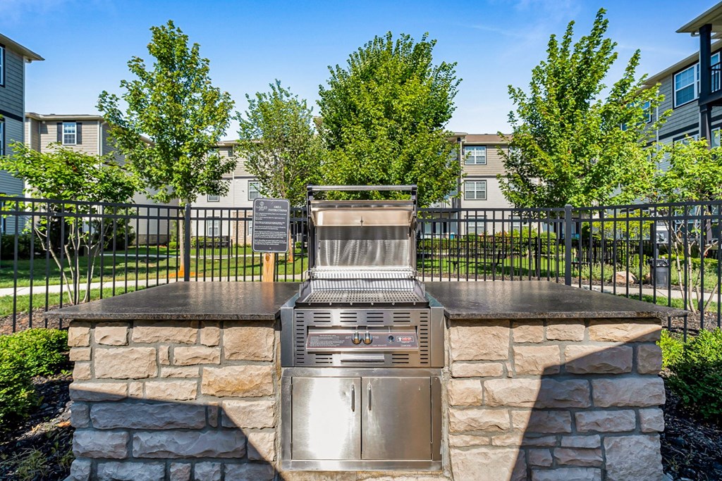 A stone fireplace with a metal grate in front of a fence and trees.