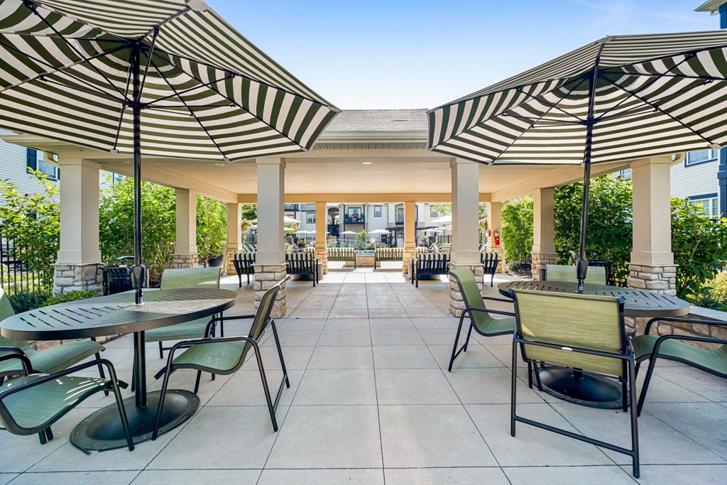 A patio with tables and chairs under striped umbrellas.