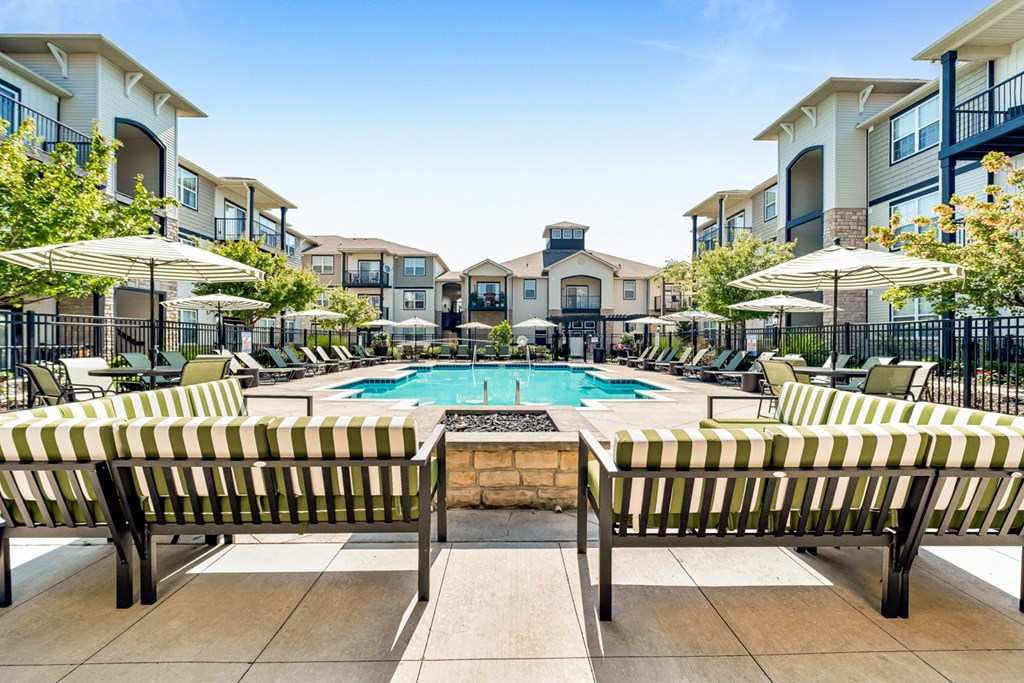 A pool surrounded by a striped bench and umbrellas with apartment buildings in the background.