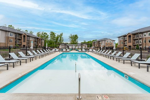 A large swimming pool surrounded by sun loungers and apartment buildings.