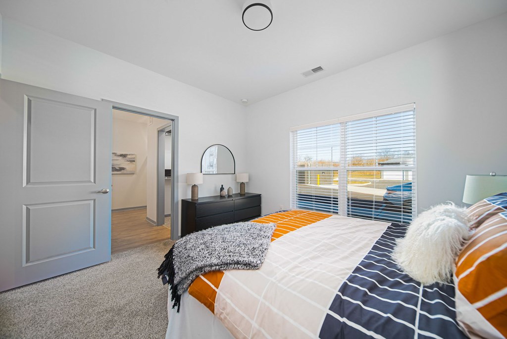 A bedroom with a bed, a nightstand, and a window with blinds.