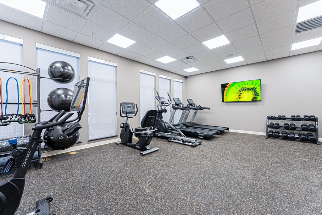 A gym with a variety of equipment including a stationary bike, treadmill, and weights.