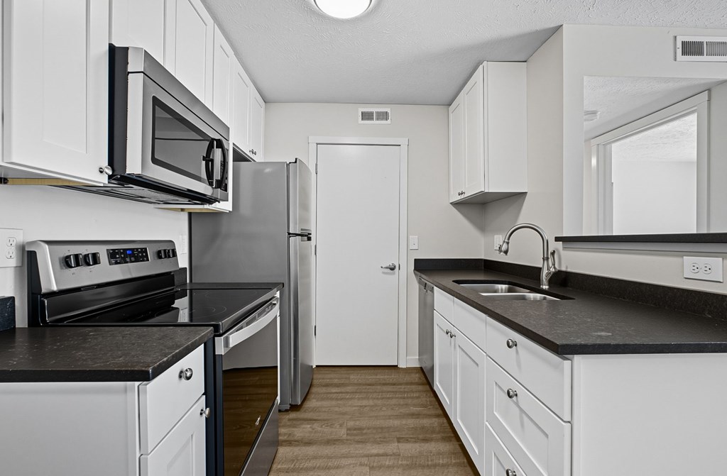 A kitchen with white cabinets and black countertops.