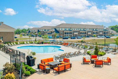 an outdoor pool with orange chairs and tables and a building in the background