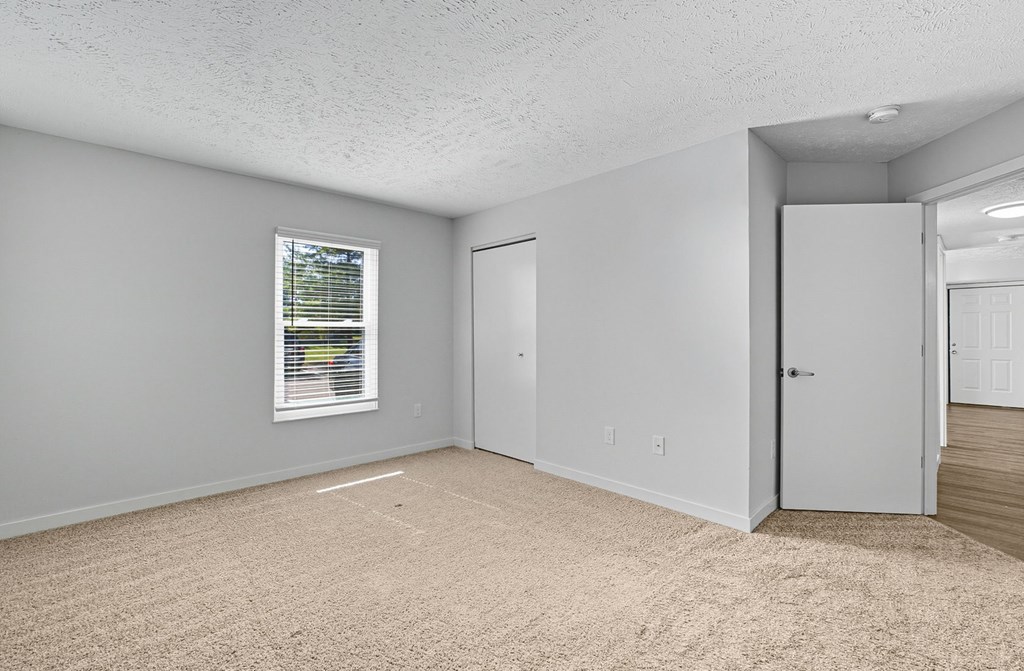 A room with a carpeted floor, a window with blinds, and a door.