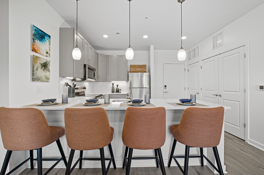 A modern kitchen with a white color scheme and three brown chairs.