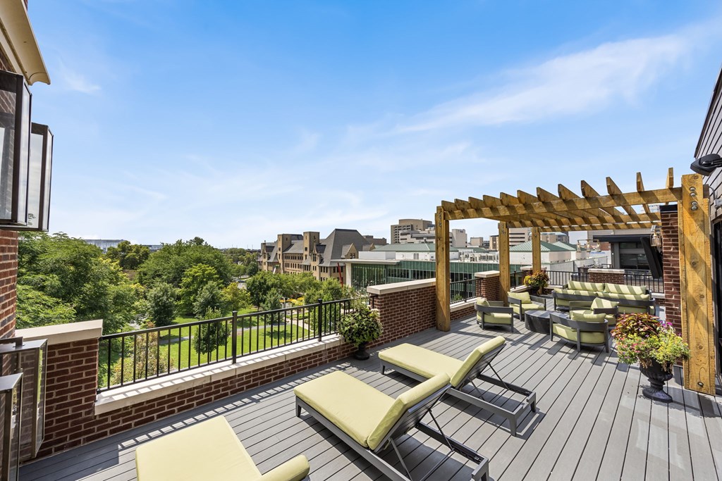 A wooden deck with a pergola and lounge chairs overlooks a cityscape.