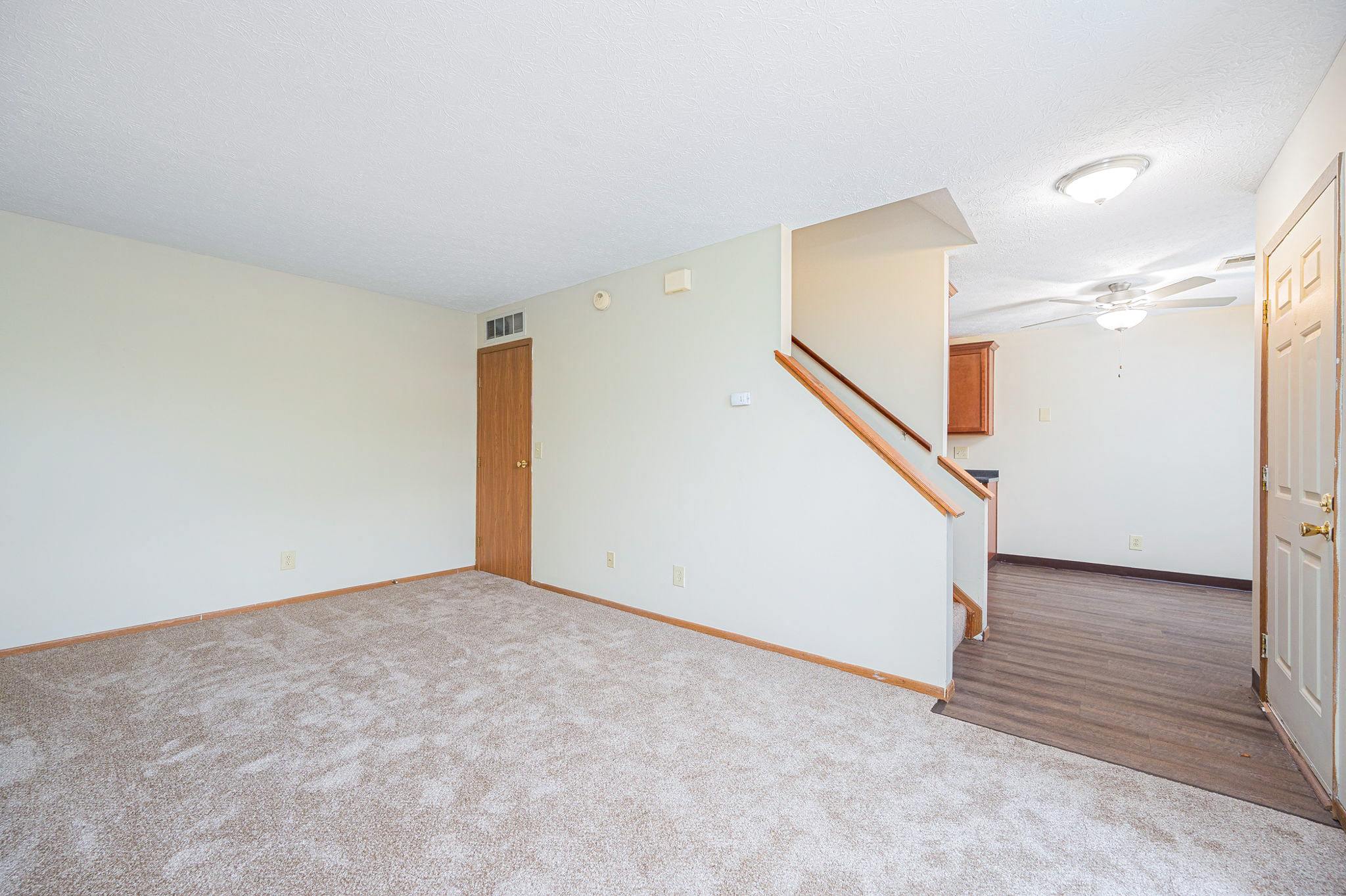 a living room with carpet and a door to a staircase