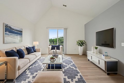 A living room with a large window and a painting of a beach scene on the wall.