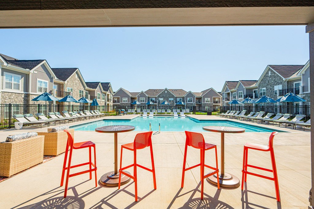 A pool surrounded by red chairs and tables.