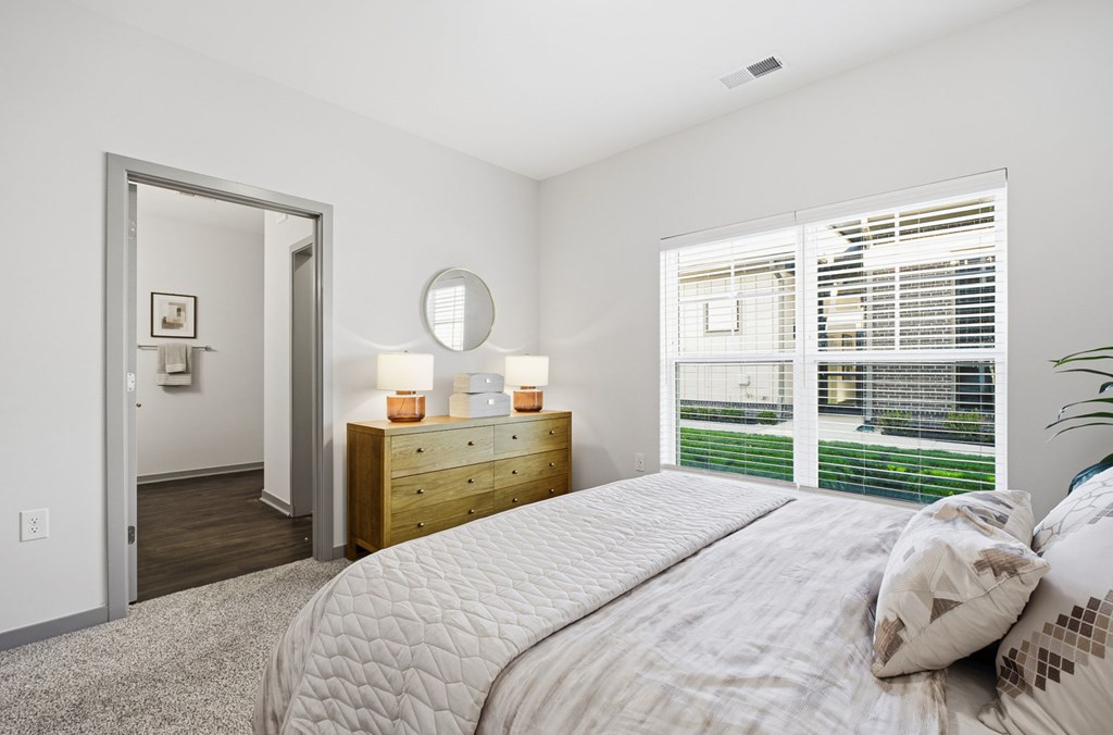 A bedroom with a large bed, a dresser, and a window with blinds.