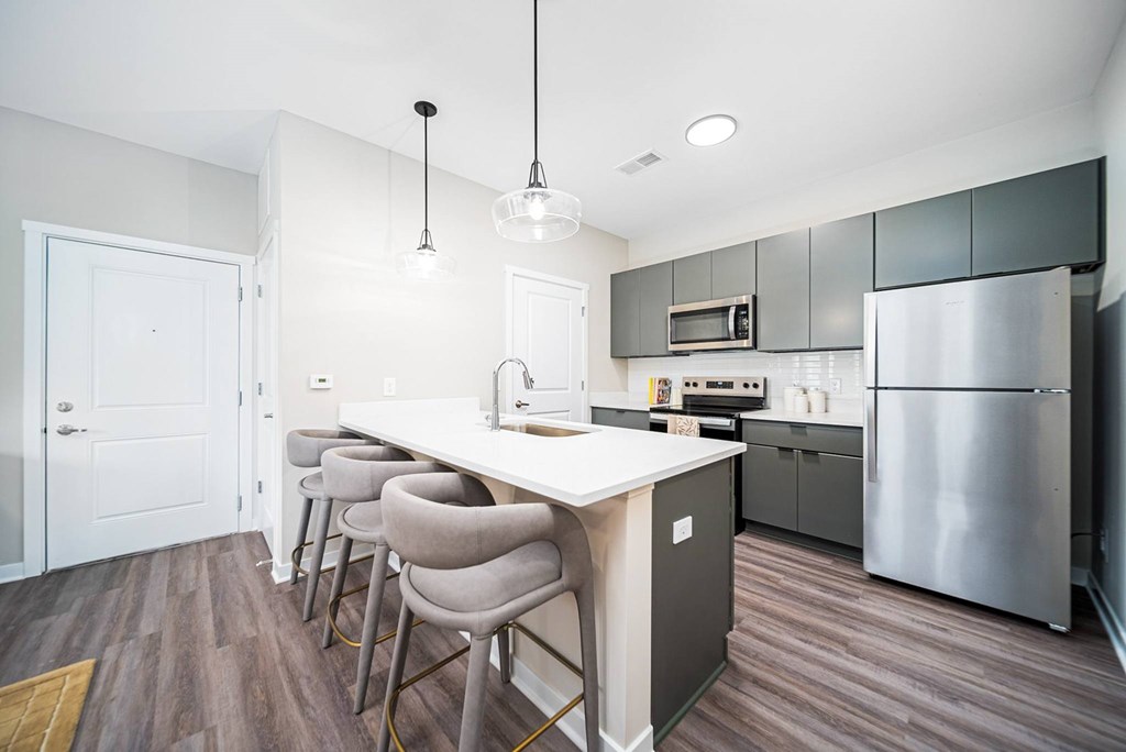 A kitchen with a white island and grey chairs.