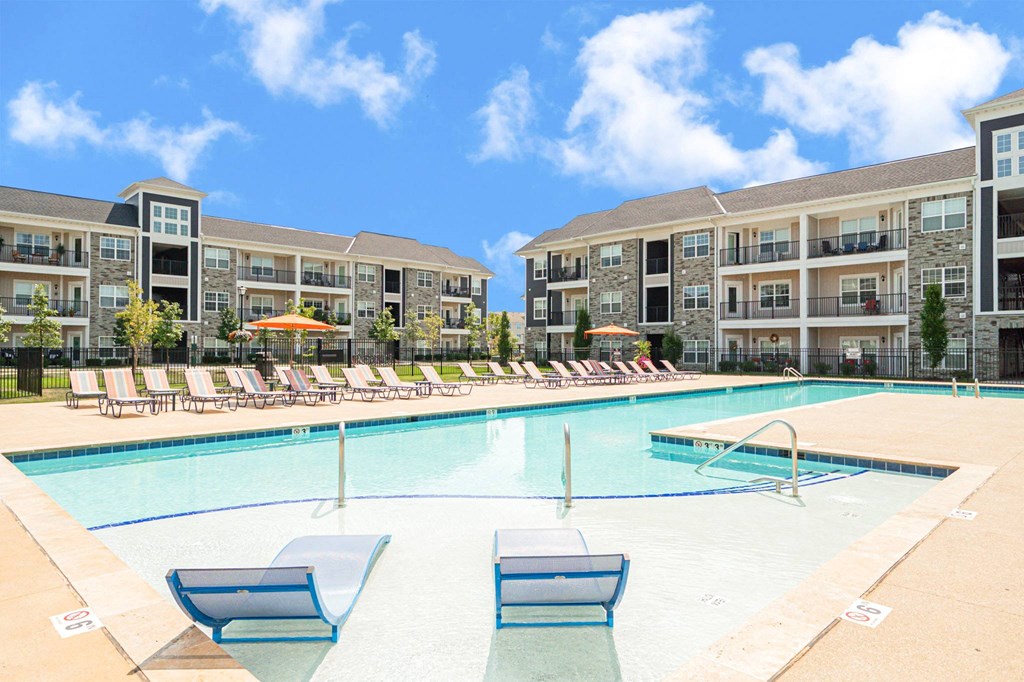 a swimming pool with lounge chairs in front of an apartment building