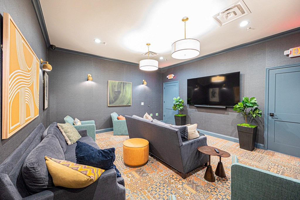 A living room with a grey couch, a yellow pillow, and a TV on the wall.