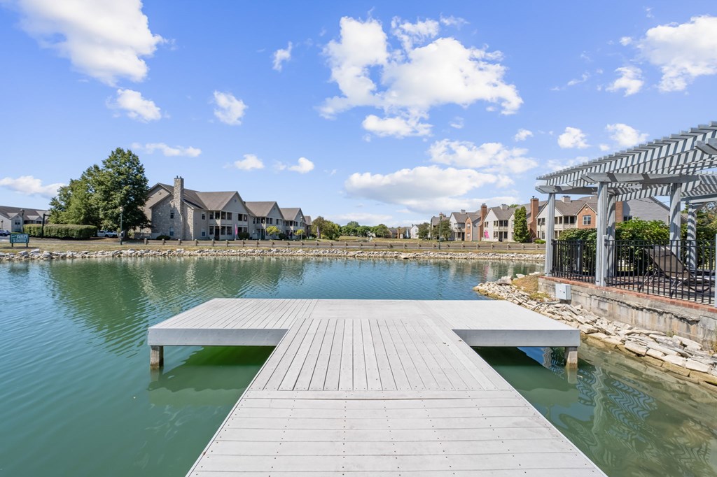 A wooden dock extends into a body of water with a residential area in the background.
