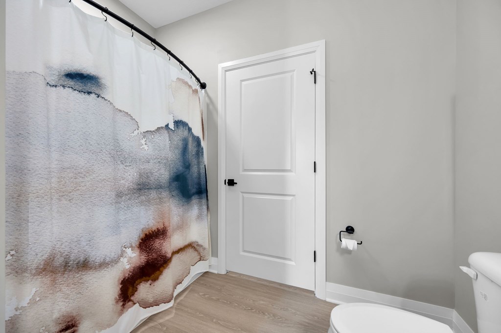 A white door is in a bathroom with a shower curtain that has blue and brown paint on it.