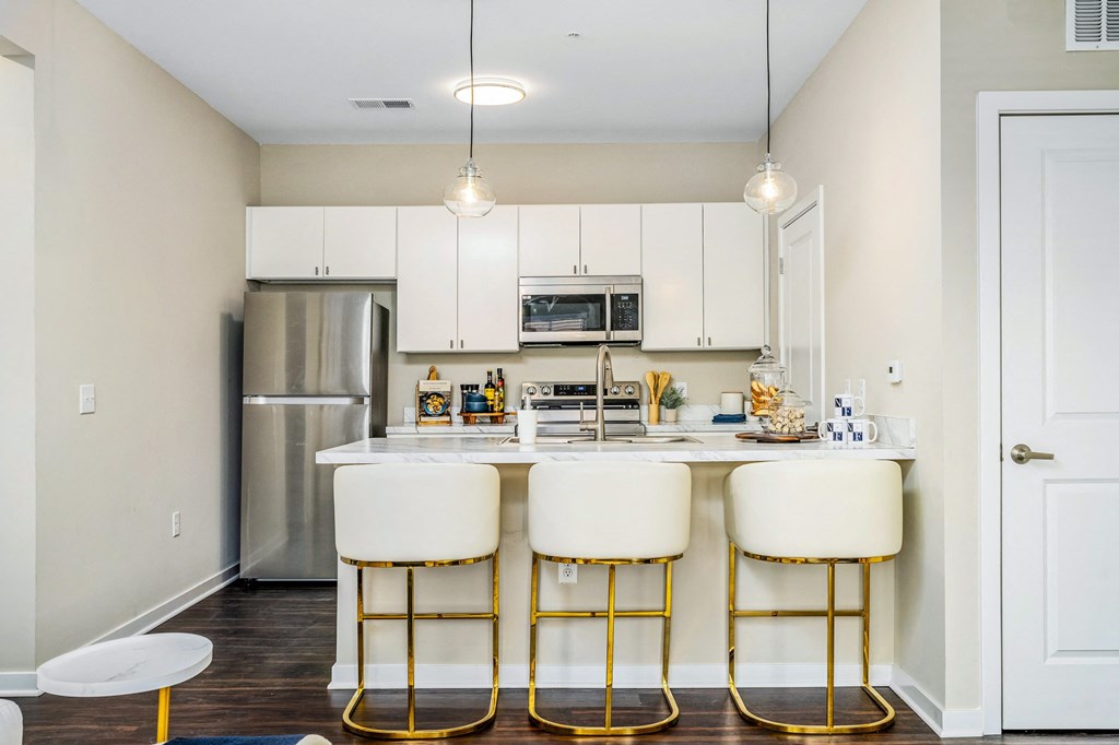 a kitchen with white cabinets and a bar with three stools