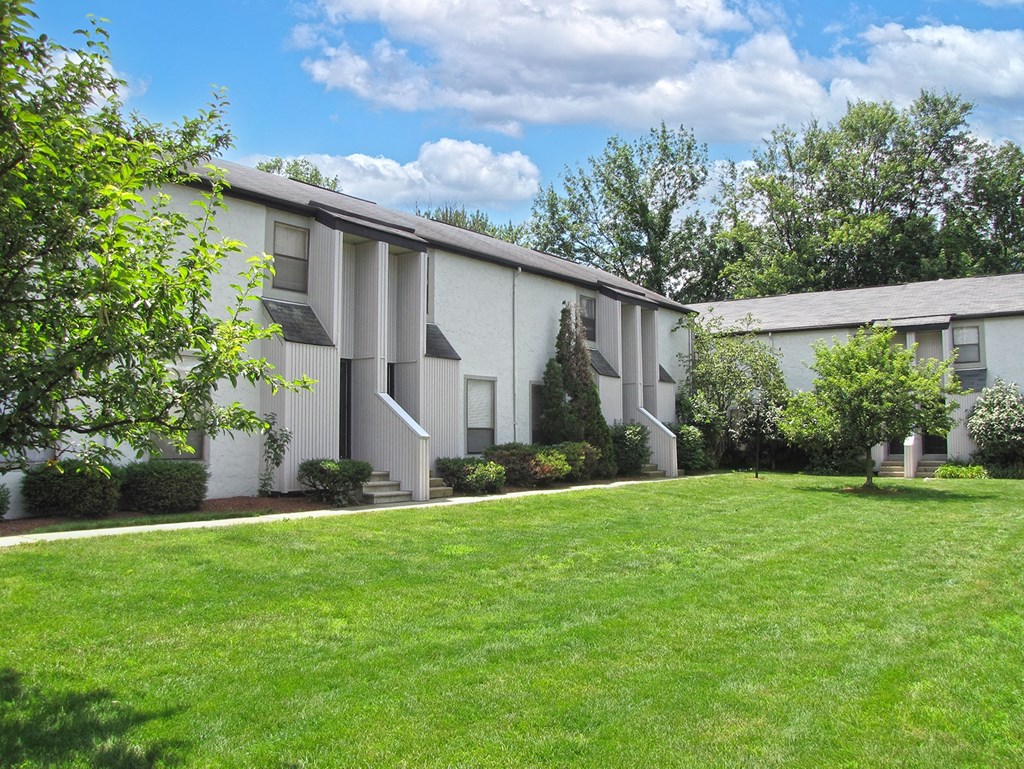 a white apartment building with a green lawn and trees