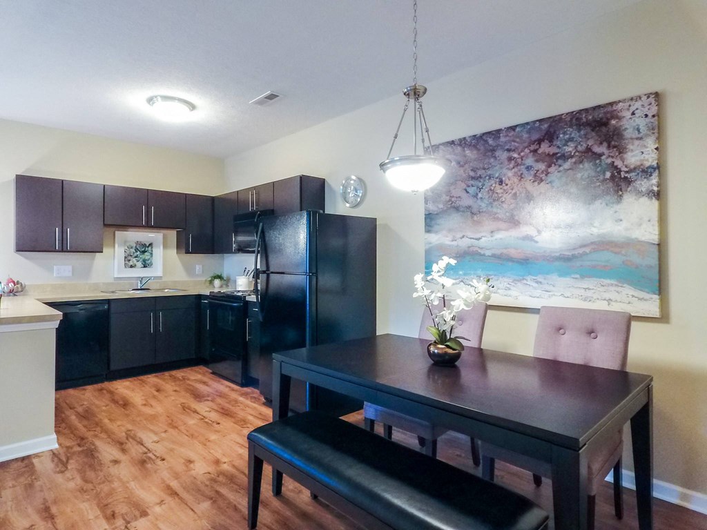 a kitchen with dark cabinets and a table with a vase of flowers on top of it