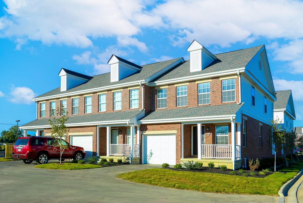 A red car is parked in front of a two-story house.