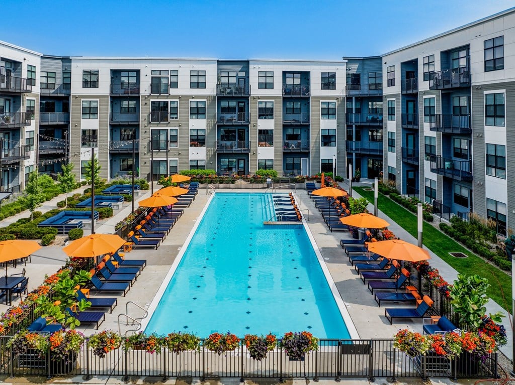 an outdoor pool with orange umbrellas in front of an apartment building
