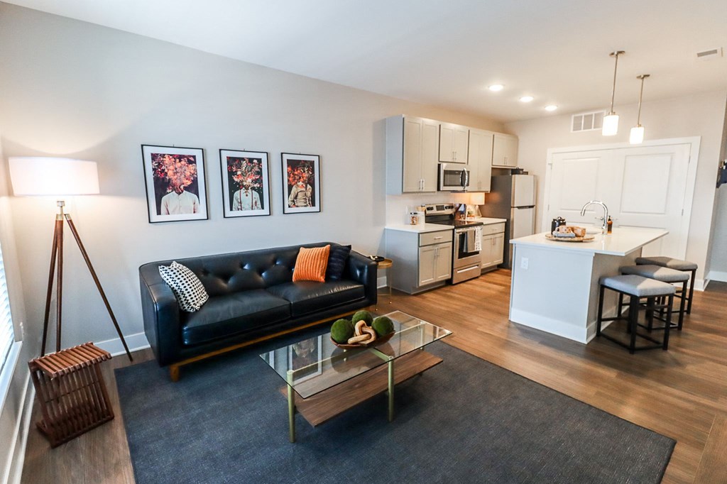 a living room with a black leather couch and a glass coffee table in front of a kitchen